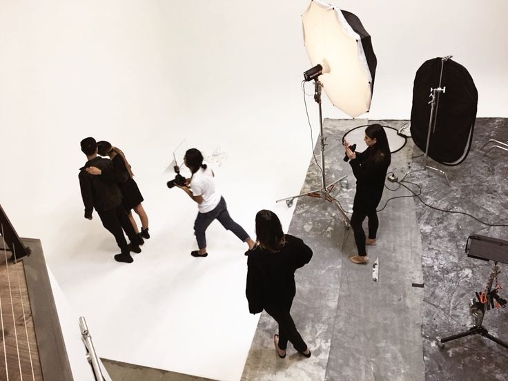 several people are standing in front of a white backdrop and lighting equipment, one person is holding a camera