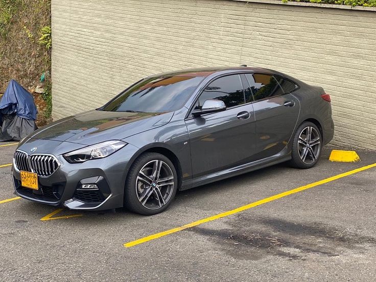 a grey bmw car parked in a parking lot next to a wall and garbage can