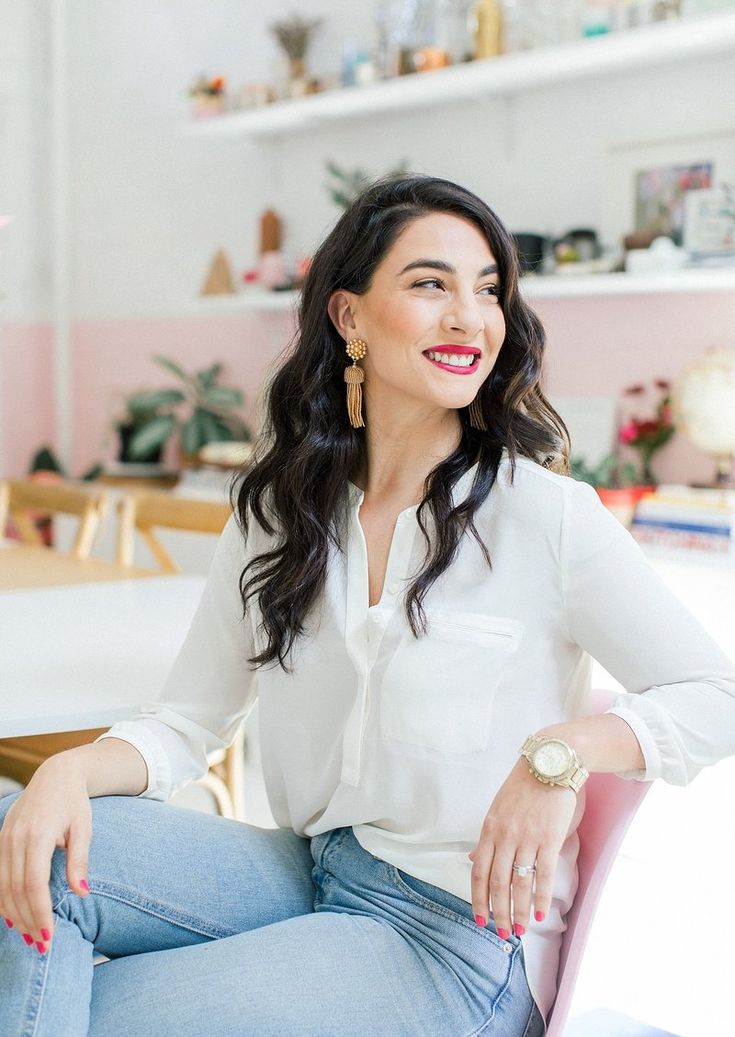 a woman sitting on top of a pink chair in a room with white walls and shelves