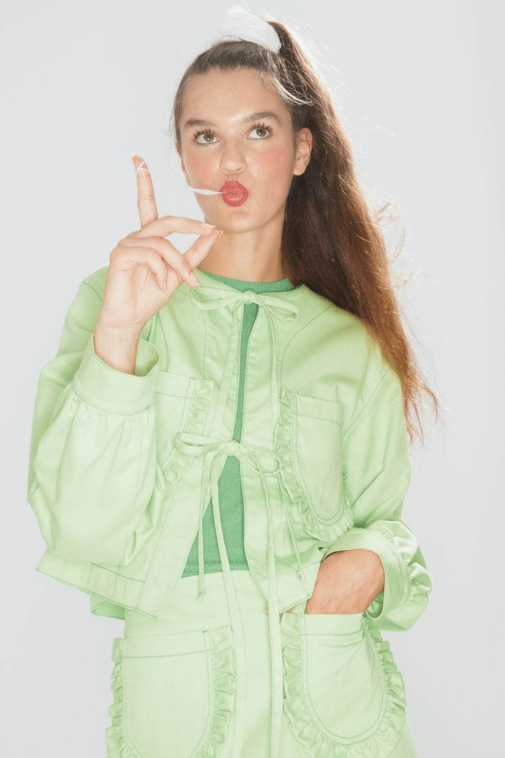 a woman with long hair wearing a green jacket and holding her finger up in the air