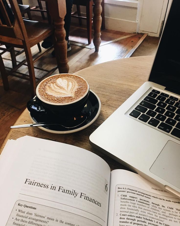 an open book with a cappuccino on it next to a laptop computer