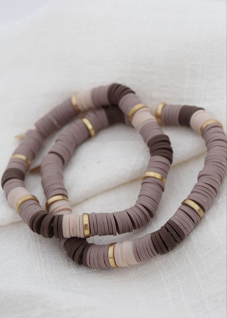 three necklaces are sitting on top of a white cloth covered surface, one is brown and the other is beige