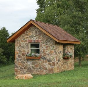 a small stone building sitting on top of a lush green field next to a forest