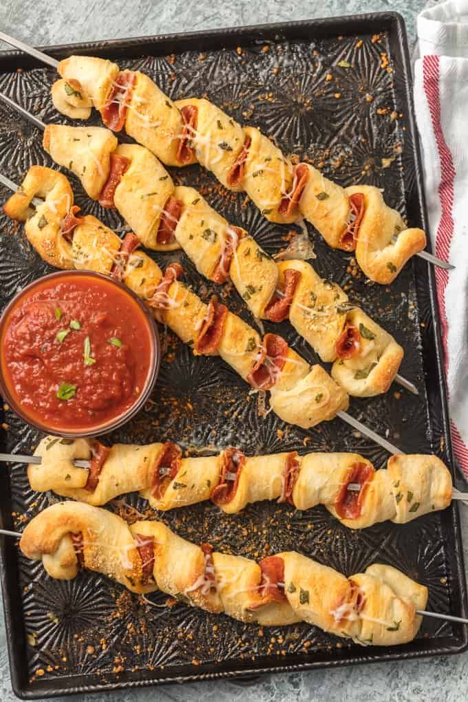 several skewers filled with meat and sauces on a black tray next to a small bowl of dipping sauce