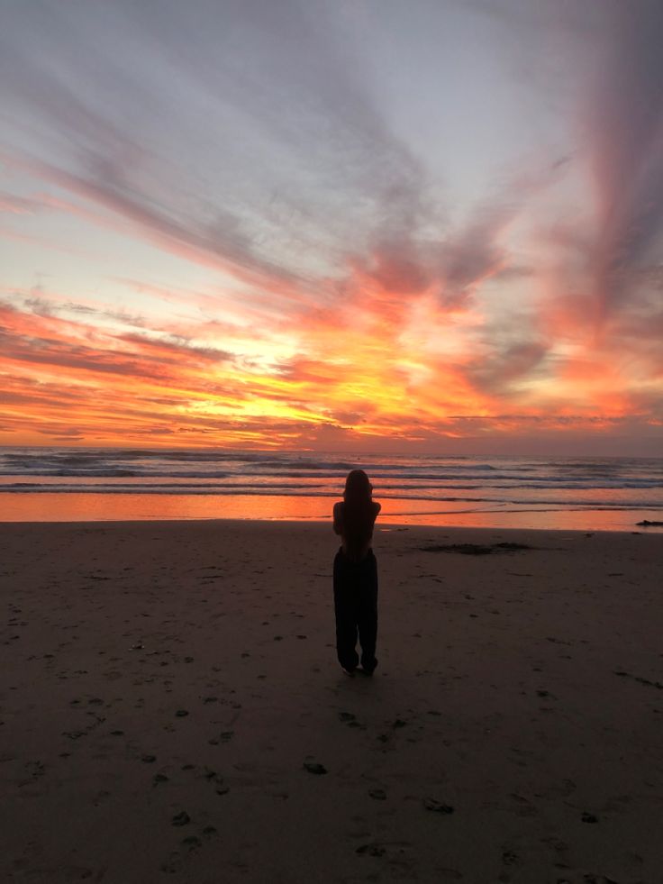 Beautiful orange, pink and yellow sunset on the beach, girl standing in forefront on the sand. Stunning sky reflecting in the still water. New Zealand Sunset, Sunset At Beach, Muriwai Beach, Yellow Clouds, Beach Clouds, Water Girl, Auckland New Zealand, Red Sky, Sunset Beach