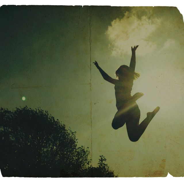 a person jumping up into the air with their arms in the air and trees behind them