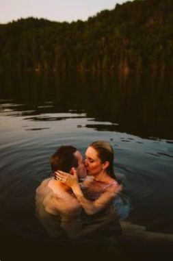 a man and woman are in the water hugging each other with trees in the background