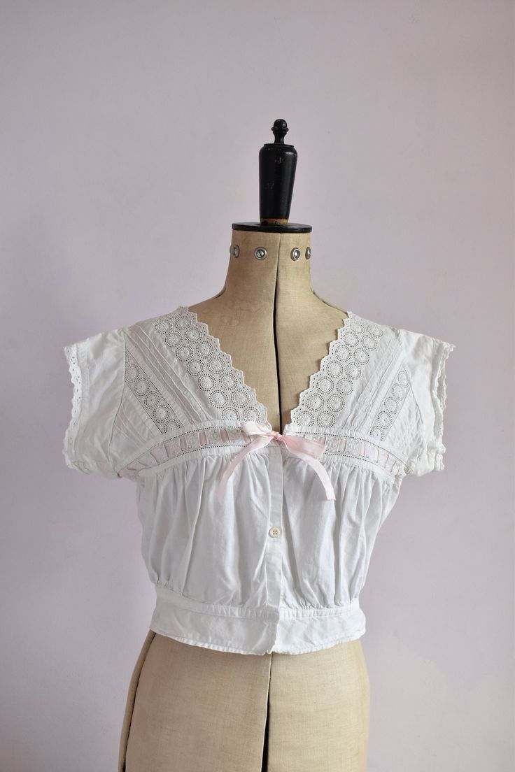 Vintage antique Victorian cotton cover blouse. Embroidered floral pattern on yoke. Scalloped neckline and around arm holes. Drawstring bust with pink ribbon. Plastic button down the front. Cinches in at the waistband with peplum. Excellent vintage condition.  Size small. Measurements:  Strap to strap: 16" Bust: 35" Waist: 26" at waistband at last fastening could be worn open up to 28" comfortably Length: 17" from top of shoulder Short Sleeve Delicate Lace Tops For Summer, Delicate Lace Short Sleeve Summer Tops, Vintage Cotton V-neck Blouse, Vintage Lace Trim Camisole Top, Vintage Camisole Top For Daywear, Fitted Cotton Lace Top With Ruffles, Daywear V-neck Top With Broderie Anglaise, V-neck Broderie Anglaise Top For Daywear, Fitted Feminine Cotton Peasant Top