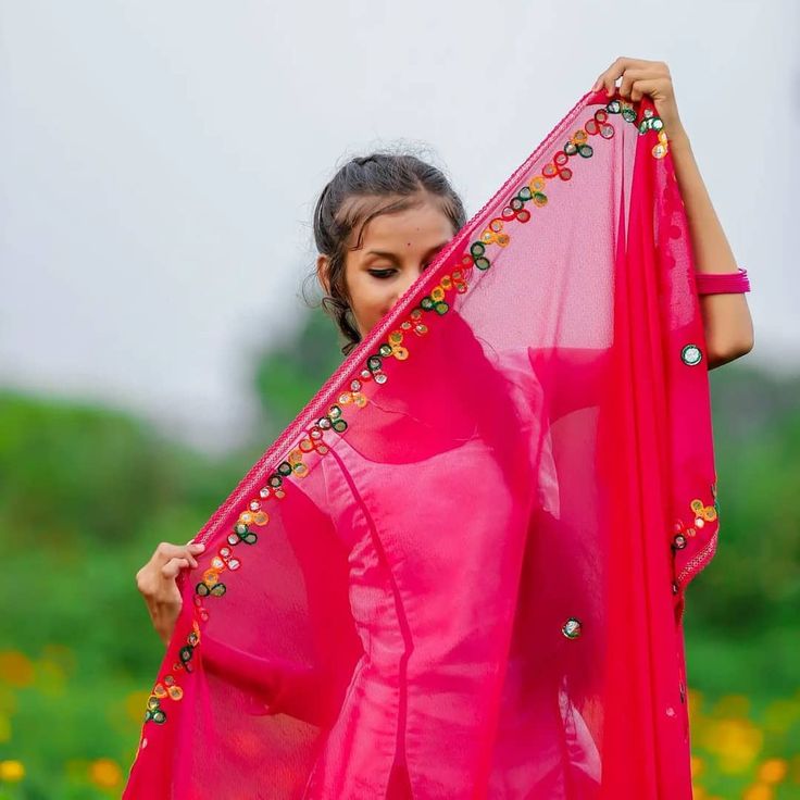 a woman in a pink sari is holding up a piece of cloth with beads on it