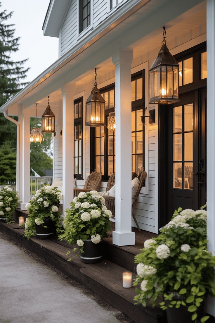 the front porch is lit up with lanterns and flowers on each planter, along with potted hydrangeas