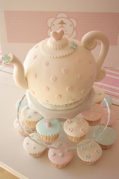 cupcakes and muffins are arranged in front of a teapot on a cake stand