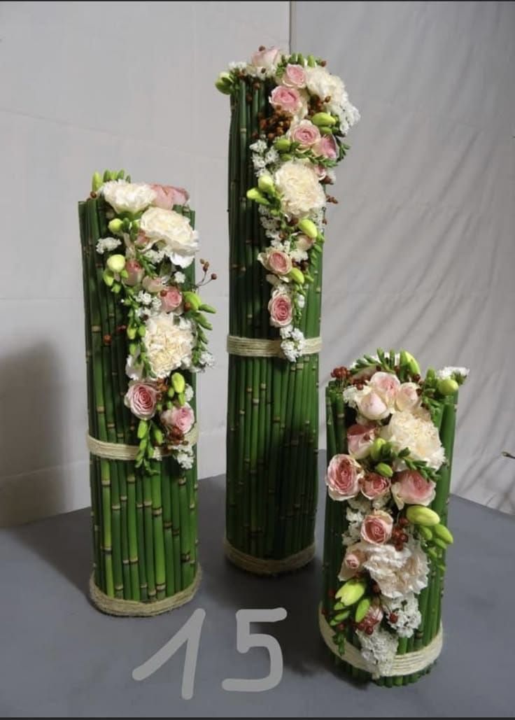 three tall vases with flowers and bamboo stems