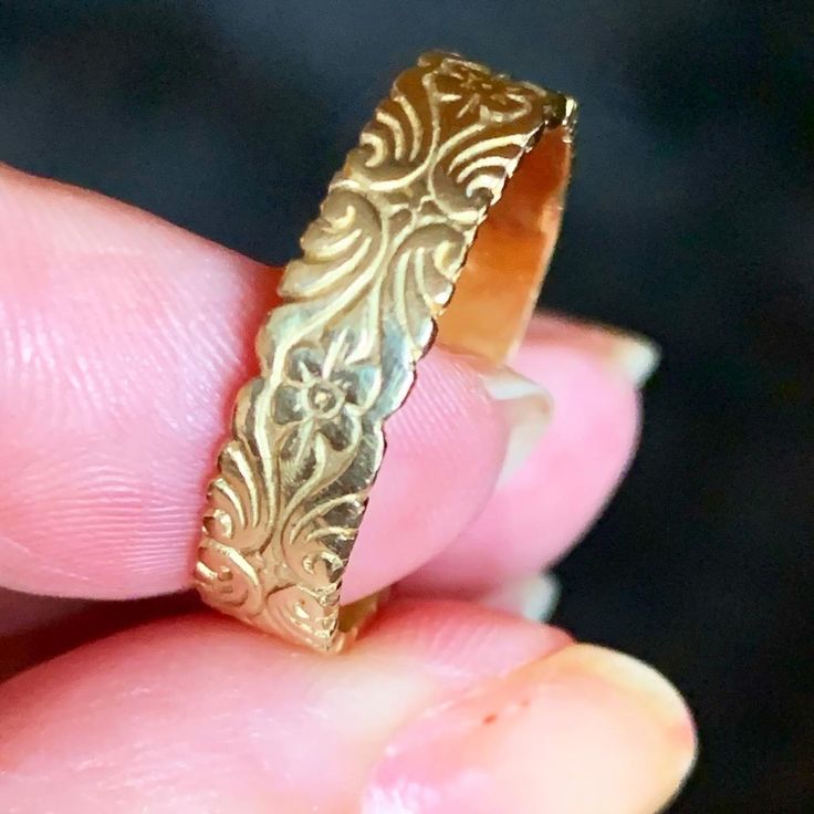 a close up of a person holding a gold ring in their left hand and wearing a wedding band with filigrees on it