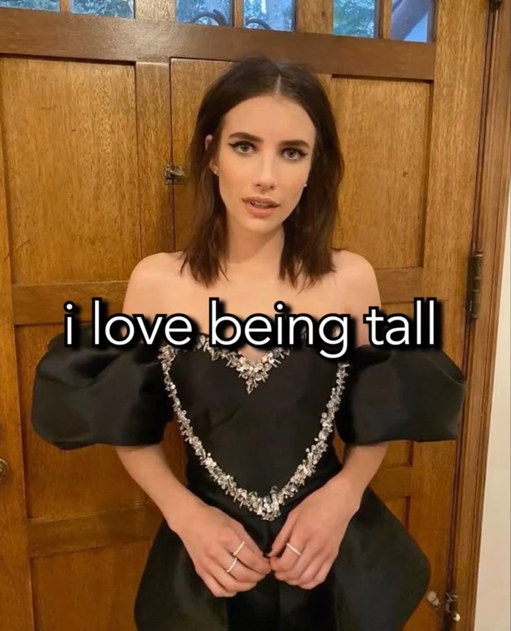 a woman standing in front of a wooden door wearing a black dress with the words i love being tall on it