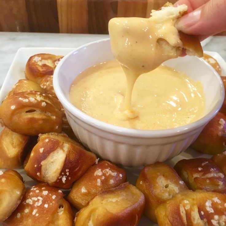 a person dipping some food into a small white bowl on top of a plate with pretzels