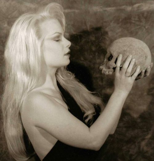 a woman with long blonde hair holding a skull in her right hand and looking at it