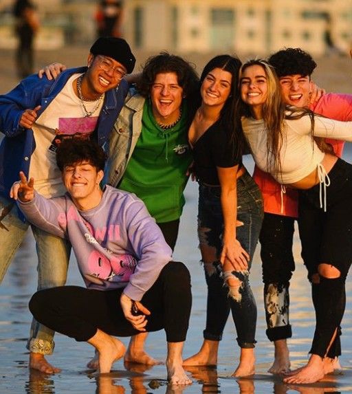 a group of young people standing next to each other on a wet beach with buildings in the background