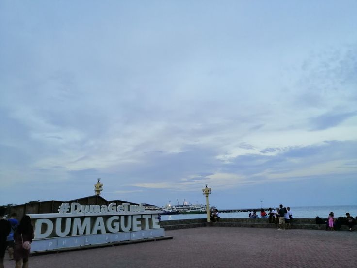 people are walking around in front of the sign that says dumagettti on it