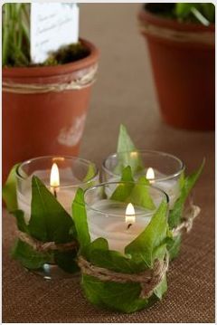 three glass candles with green leaves and twine around them on a brown table cloth