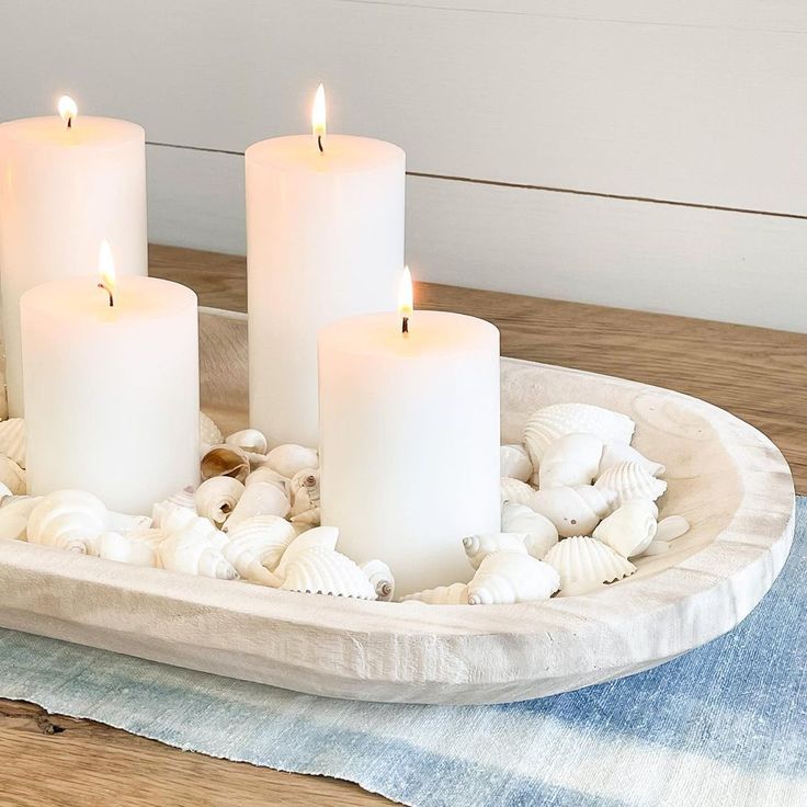 three white candles sitting on top of a tray filled with seashells