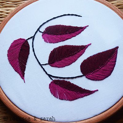 a close up of a embroidery on a piece of cloth with red leaves in it