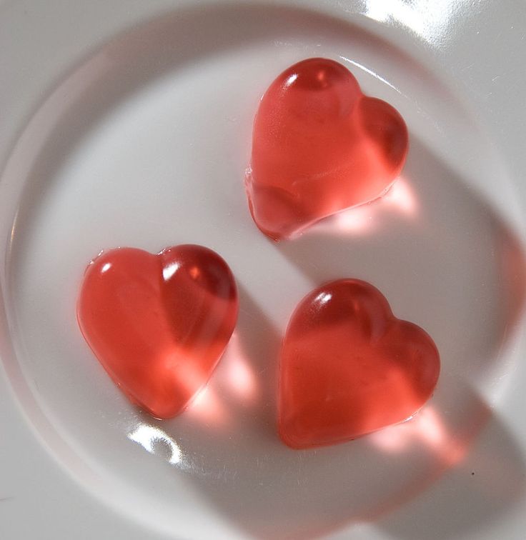 three heart shaped candies sitting on top of a white plate with shadows coming from them