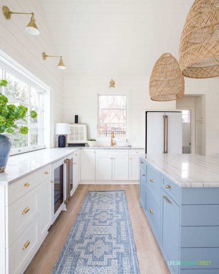 a kitchen with white cabinets and blue rugs on the floor, along with wicker baskets hanging from the ceiling