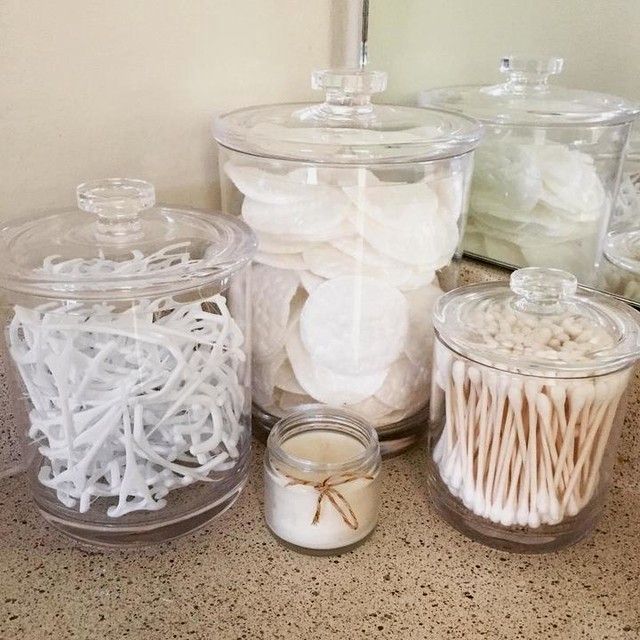 there are many jars with different types of items in them on the counter top, including cotton swabs and toothpicks