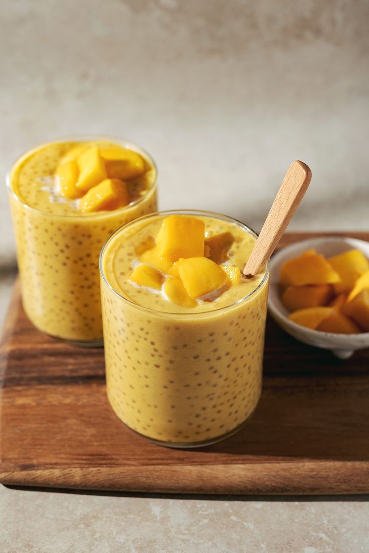 two glasses filled with mango custard on top of a wooden tray