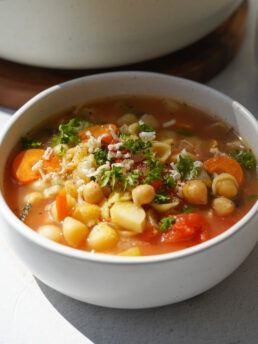 a white bowl filled with soup next to a pot full of food on top of a table