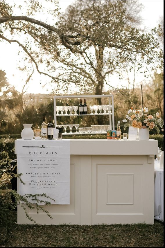 an outdoor bar is set up with bottles and wine glasses on the counter, near a tree