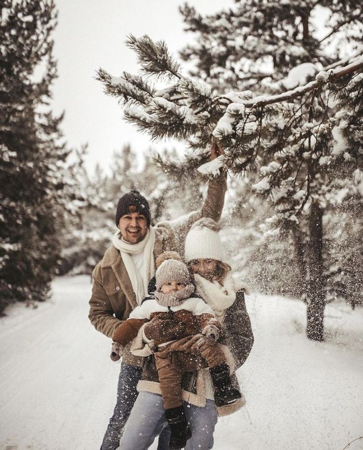 two adults and a child standing in the snow near a pine tree on a snowy day