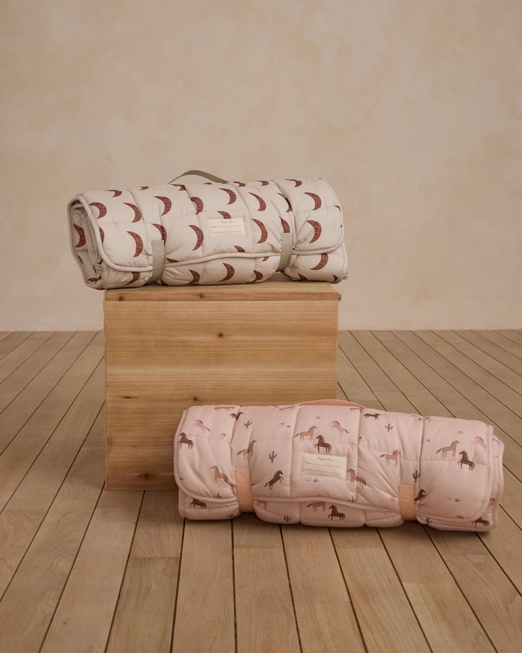 three folded baby blankets sitting on top of a wooden box next to a sleeping bag