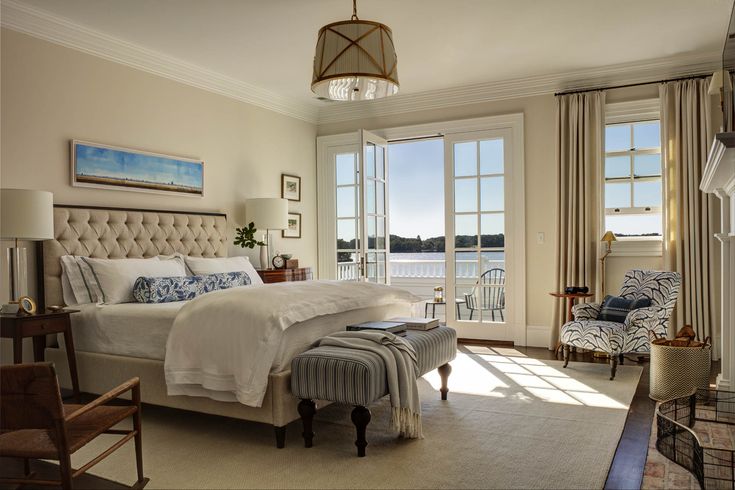 a bedroom with a large bed and two chairs in front of a window overlooking the water