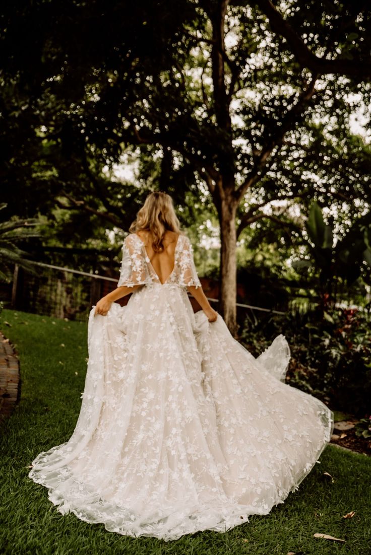 a woman in a wedding dress standing on the grass with her back to the camera