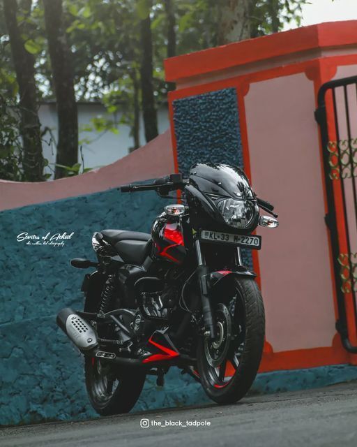 a black motorcycle parked in front of a red and blue wall next to a fence