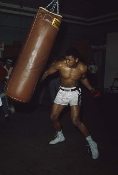 a man with no shirt and shorts is boxing in a dark room, holding a brown punching bag