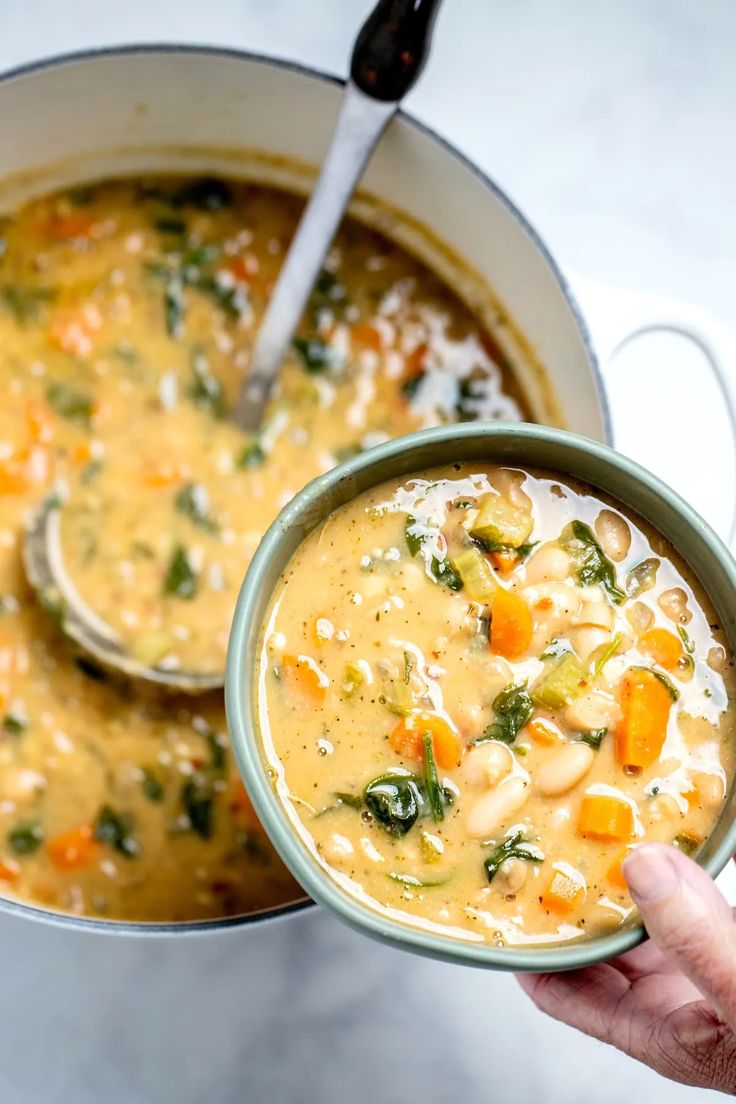 a person holding a bowl of soup with two spoons in it and another pot full of soup