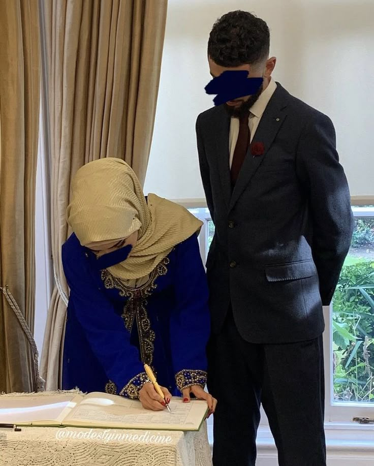 a man and woman standing next to each other in front of a table with a book on it