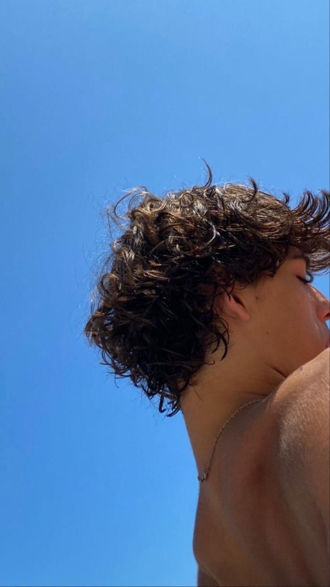 a young man with curly hair is flying a kite in the blue sky on a sunny day