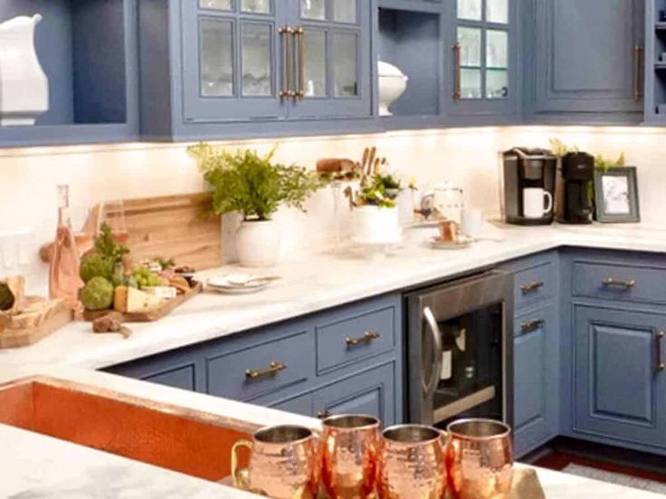 a kitchen with blue cabinets and white counter tops is pictured in this image, there are three cups on the counter