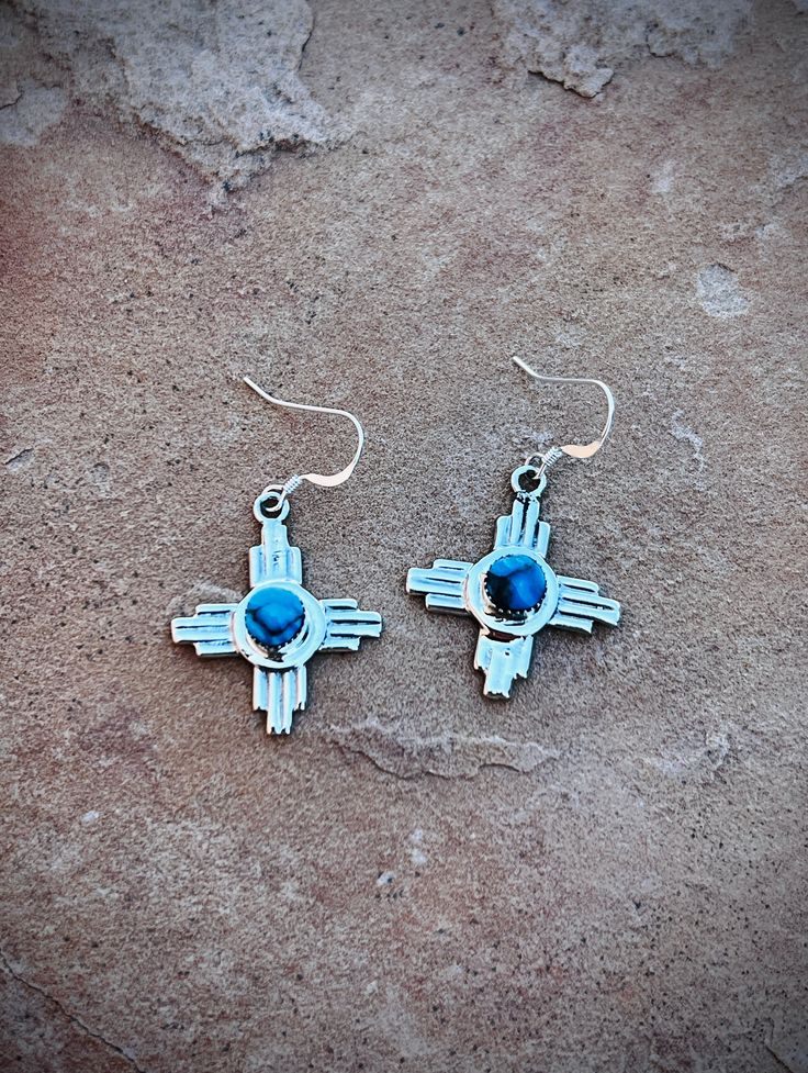 Experience the beauty of New Mexico with our Zia Symbol Turquoise Earrings. Handcrafted by Navajo artist Gregg Yazzie, these .925 sterling silver earrings feature the iconic Zia symbols and vibrant turquoise stones. Take a piece of Native American culture with you wherever you go. Symbolic Teardrop Jewelry With Matching Earrings, Turquoise Symbolic Round Jewelry, Artisan Blue Nickel-free Earrings, Unique Turquoise Drop Earrings, Southwestern Sterling Silver Gemstone Jewelry, Turquoise Inlay Earrings Gift, Turquoise Inlay Earrings As Gift, Artisan Turquoise Gemstone Earrings, Artisan Turquoise Jewelry With Matching Earrings