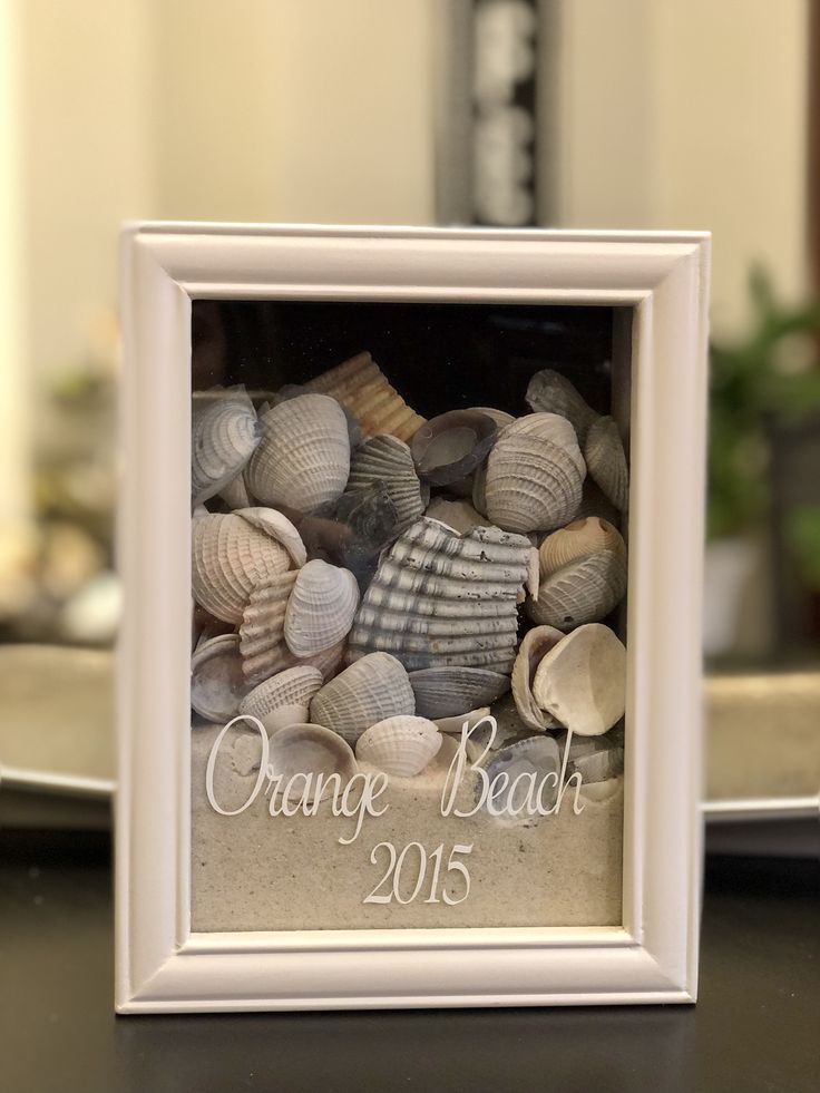 a white frame with shells in it and the words orange beach written on it is sitting on a table