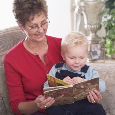 an older woman sitting on a couch reading to a young boy who is looking at a book