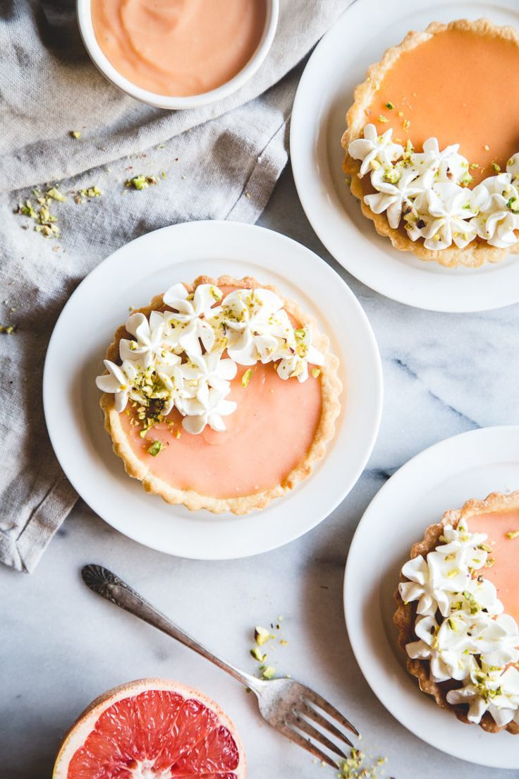 three small desserts on white plates with grapefruit and whipped cream frosting