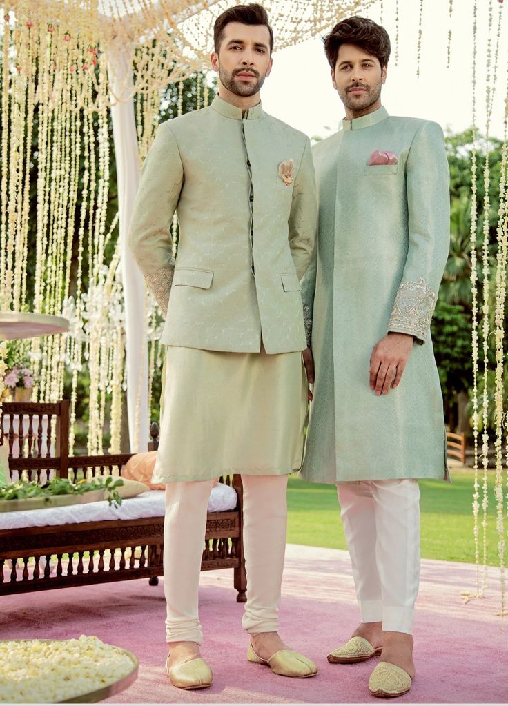 two men standing next to each other in front of a decorated area with flowers and greenery