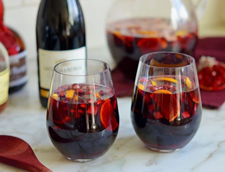 two wine glasses filled with red liquid sitting on top of a table next to bottles of wine