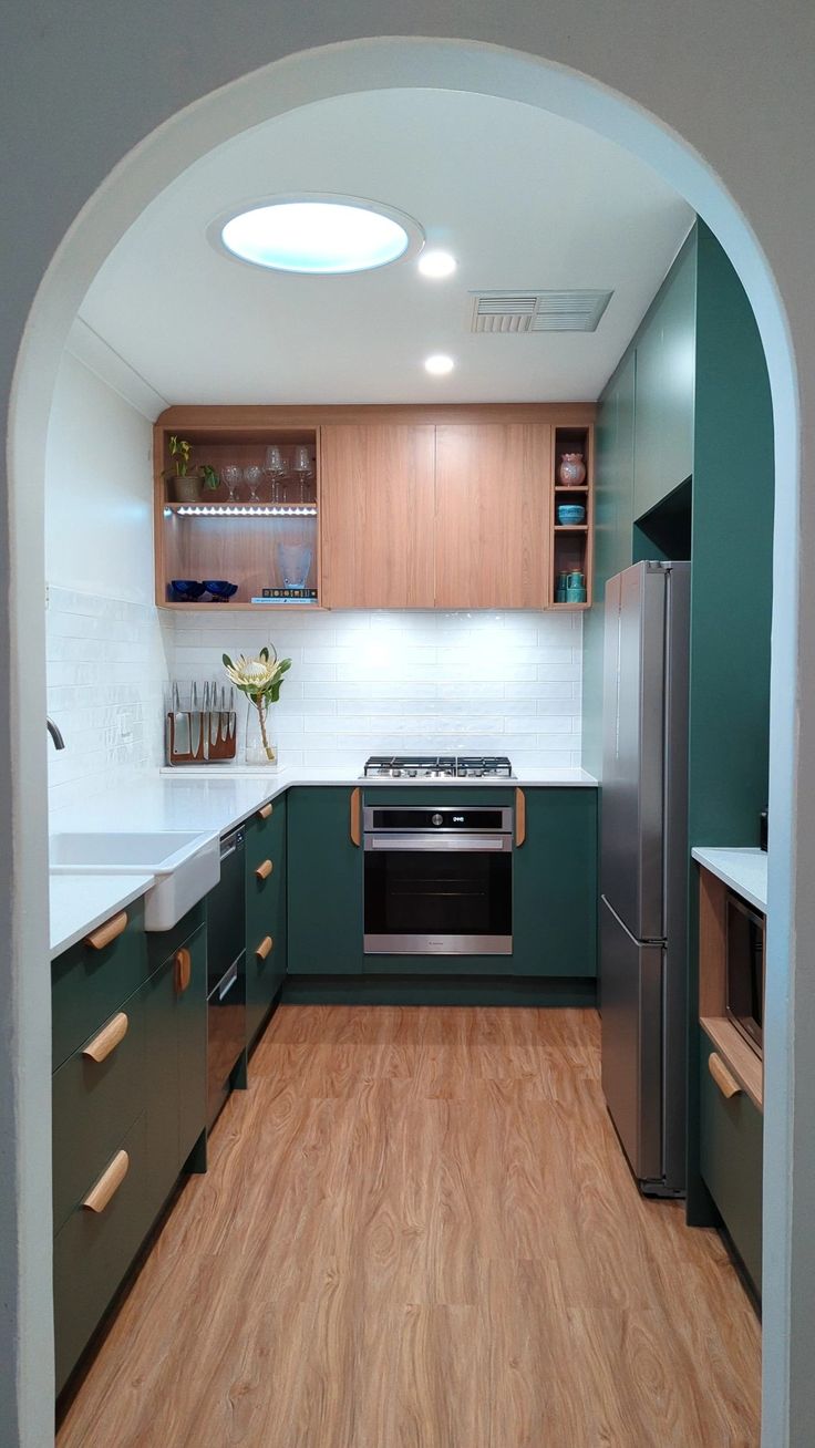 a kitchen with wood floors and green cabinets is seen through an arch in the wall