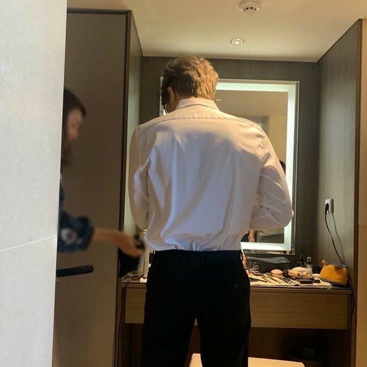 a man in a white shirt and black pants is standing in front of a mirror