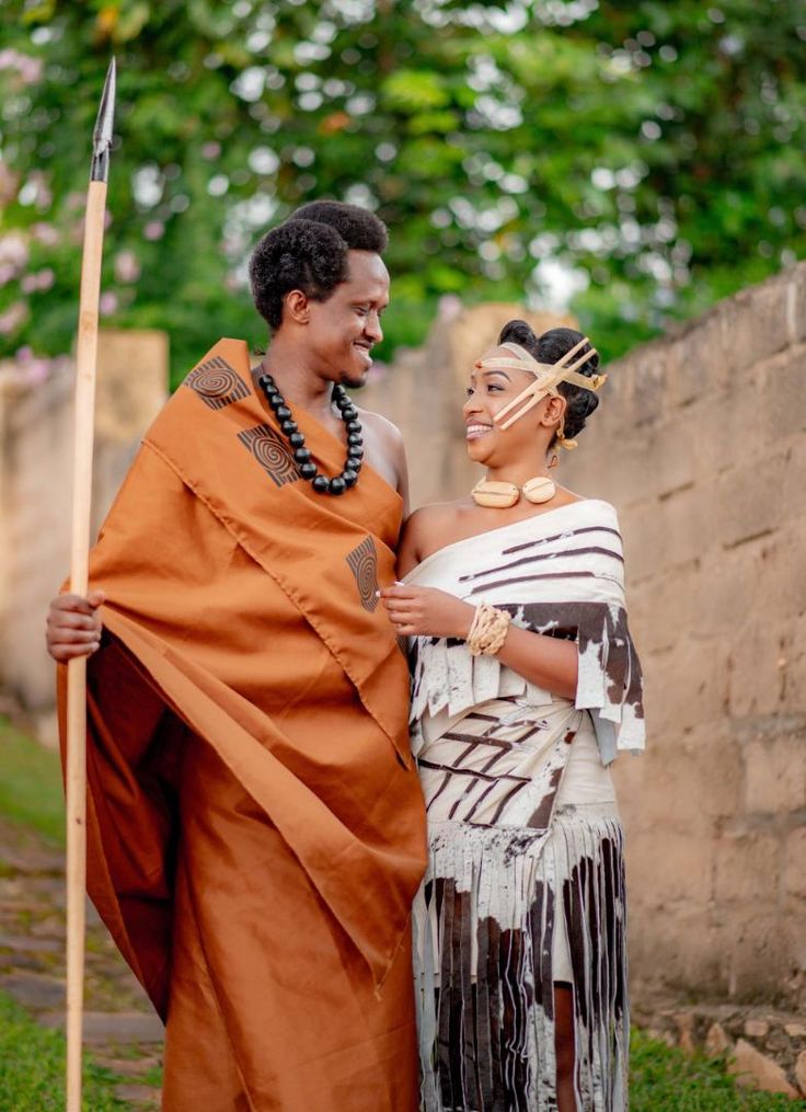 a man and woman dressed in african garb standing next to each other with a spear